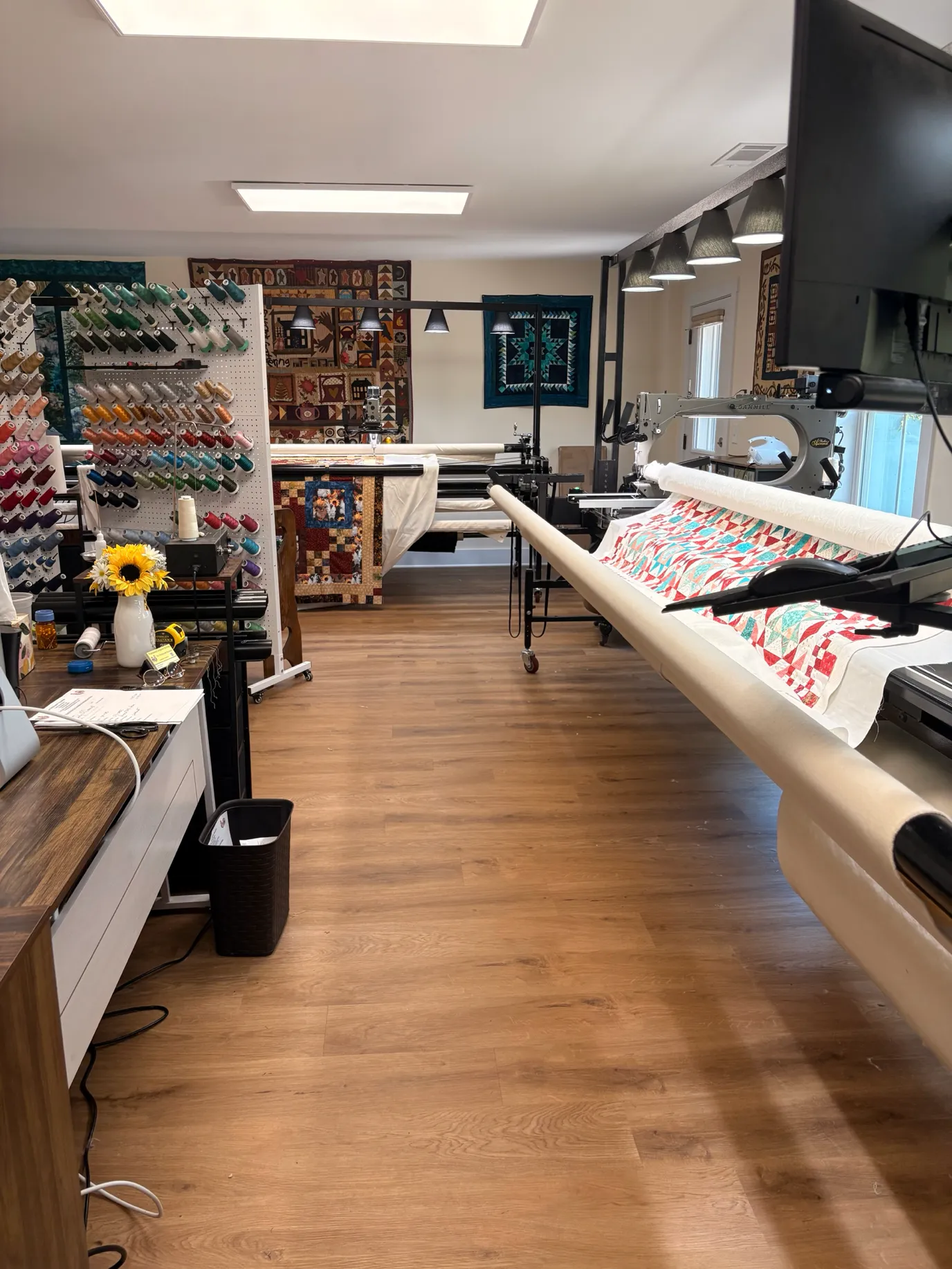The Patchwork Rooster shop interior with longarm quilting machines, thread rack, and quilts on display
